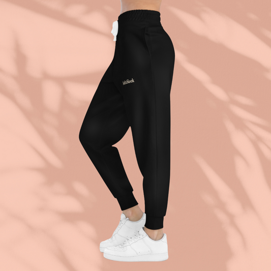 Side view of black Soft & Sleek joggers being worn with white trainers, peach background with shadows.