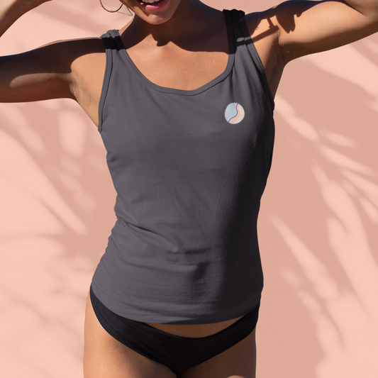 Woman in a grey Soft & Sleek lifestyle tank top with emblem on chest, posing against a peach background.