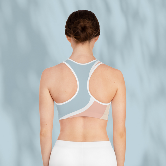 Rear view of woman wearing the same multicolour Soft & Sleek sports bra with racerback design, arms relaxed, pale blue background