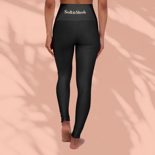 Rear view of a woman in black Soft & Sleek leggings with logo at the waistband, peach background and soft shadows.