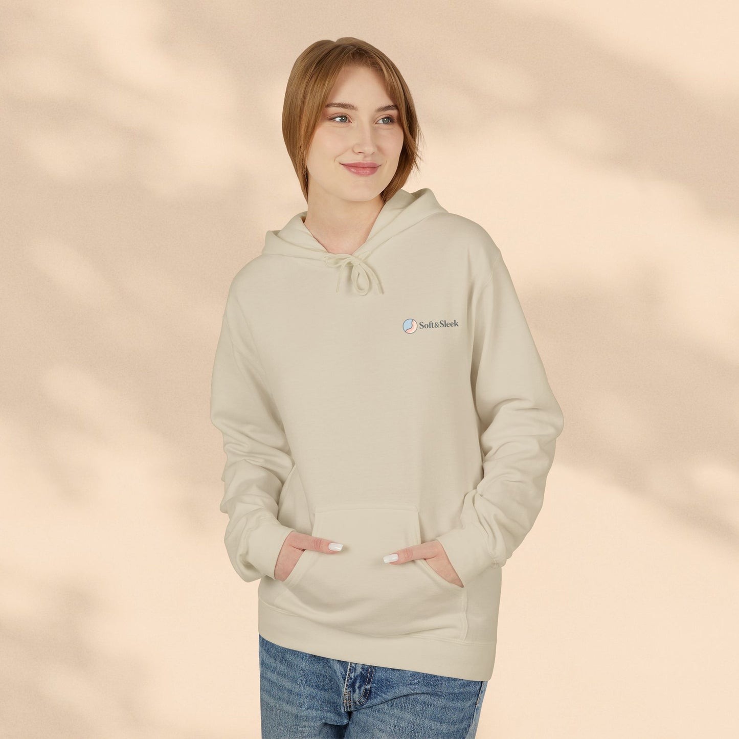 Woman wearing beige Soft & Sleek hoodie with small chest logo, hands in pocket, beige background