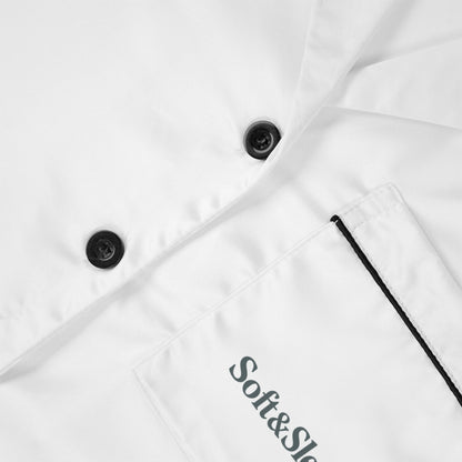 Close-up of Soft & Sleek embroidered logo on white satin fabric, showing black buttons and chest pocket trim.