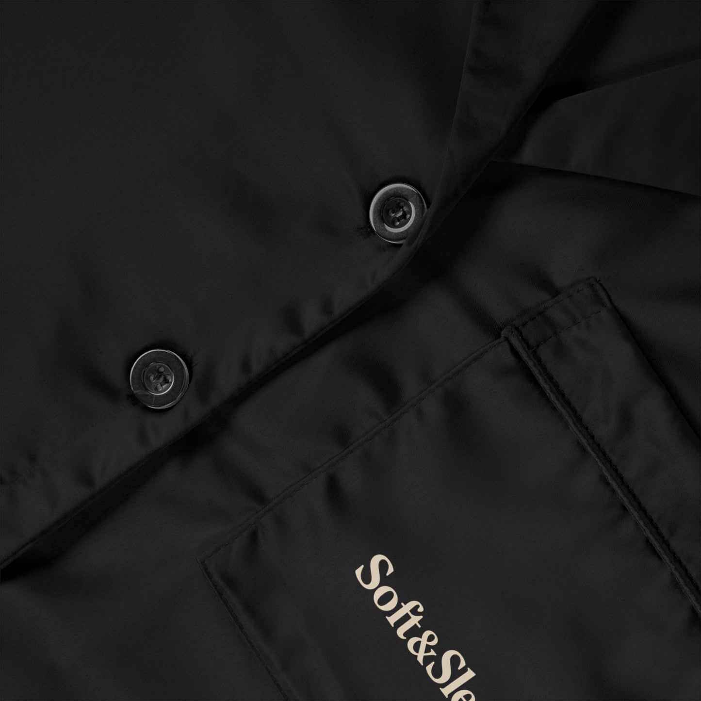 Close-up of black satin fabric with buttons and embroidered Soft & Sleek logo on chest pocket.
