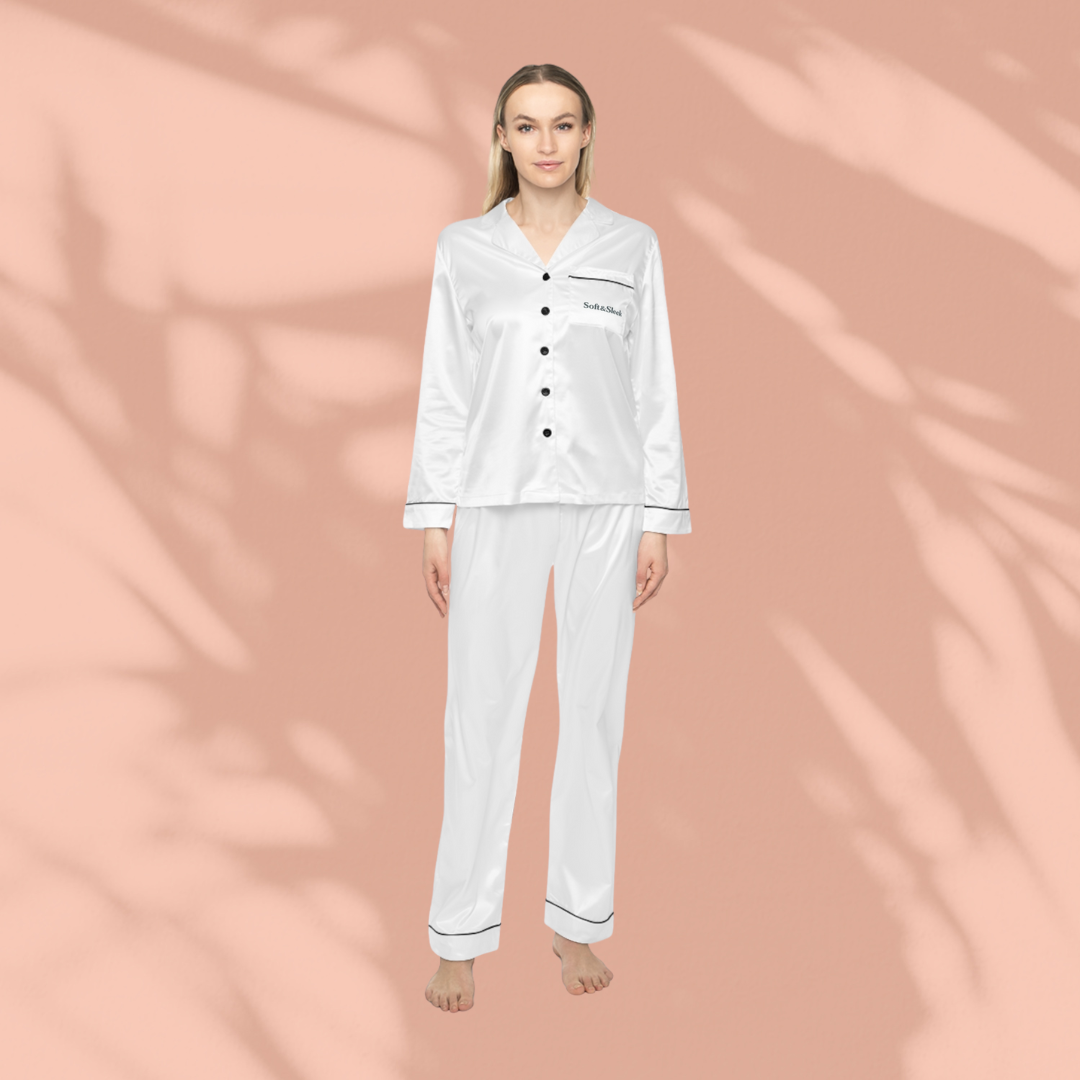 Woman standing barefoot in a white satin Soft & Sleek pyjama set with black piping, front view, peach background.