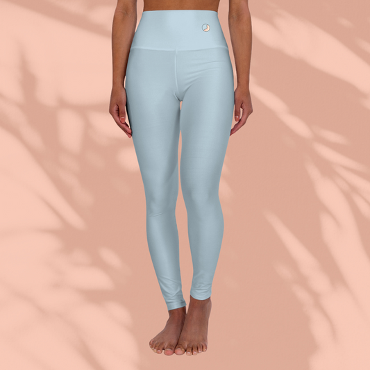 Front view of woman wearing pastel blue Soft & Sleek seamless leggings with circular emblem on waistband, barefoot, peach background