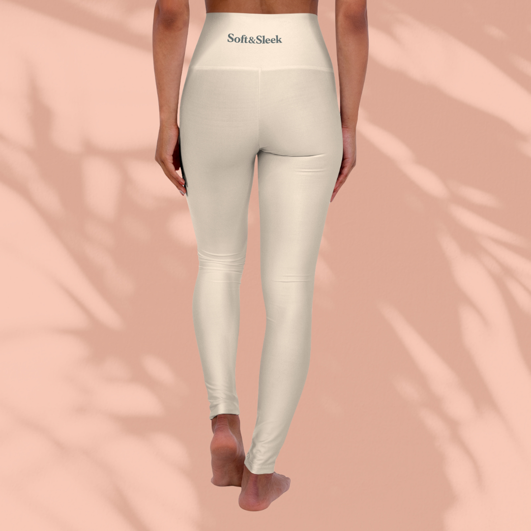 Rear view of woman in cream Soft & Sleek leggings with logo on waistband, standing barefoot against a peach background