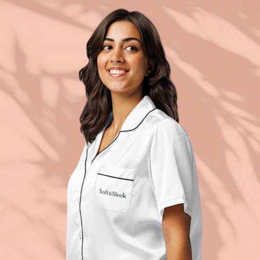 Side view of a woman smiling in a white Soft & Sleek shirt with black piping, against a peach background.