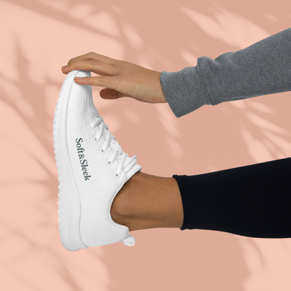 Side view of a person holding their foot up, wearing a white Soft & Sleek sneaker with the logo on the side.