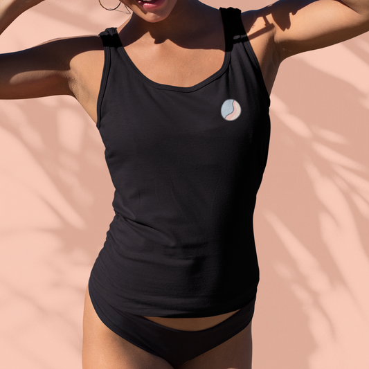 Woman wearing a black Soft & Sleek lifestyle tank top with circular emblem, stretching arms above head in sunlight, peach background.