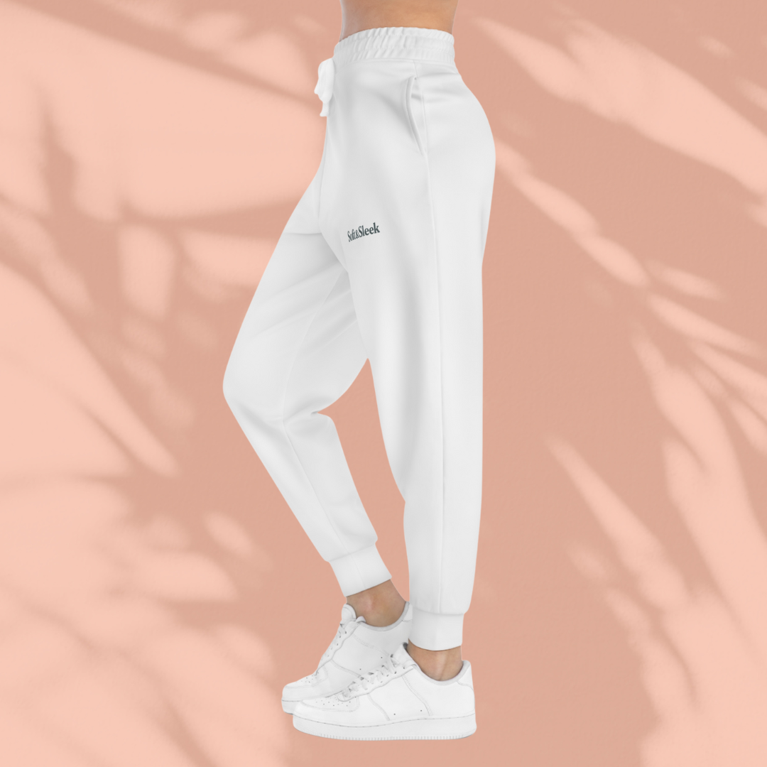 Side view of woman wearing white Soft & Sleek joggers with drawstring waist and logo on thigh, paired with white trainers, peach background