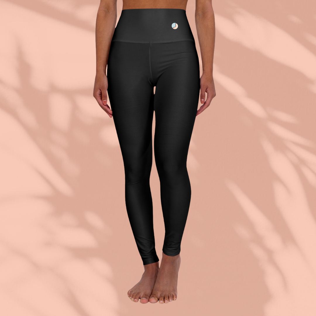 Front view of a woman wearing black Soft & Sleek high-waisted leggings, standing barefoot against a peach background.