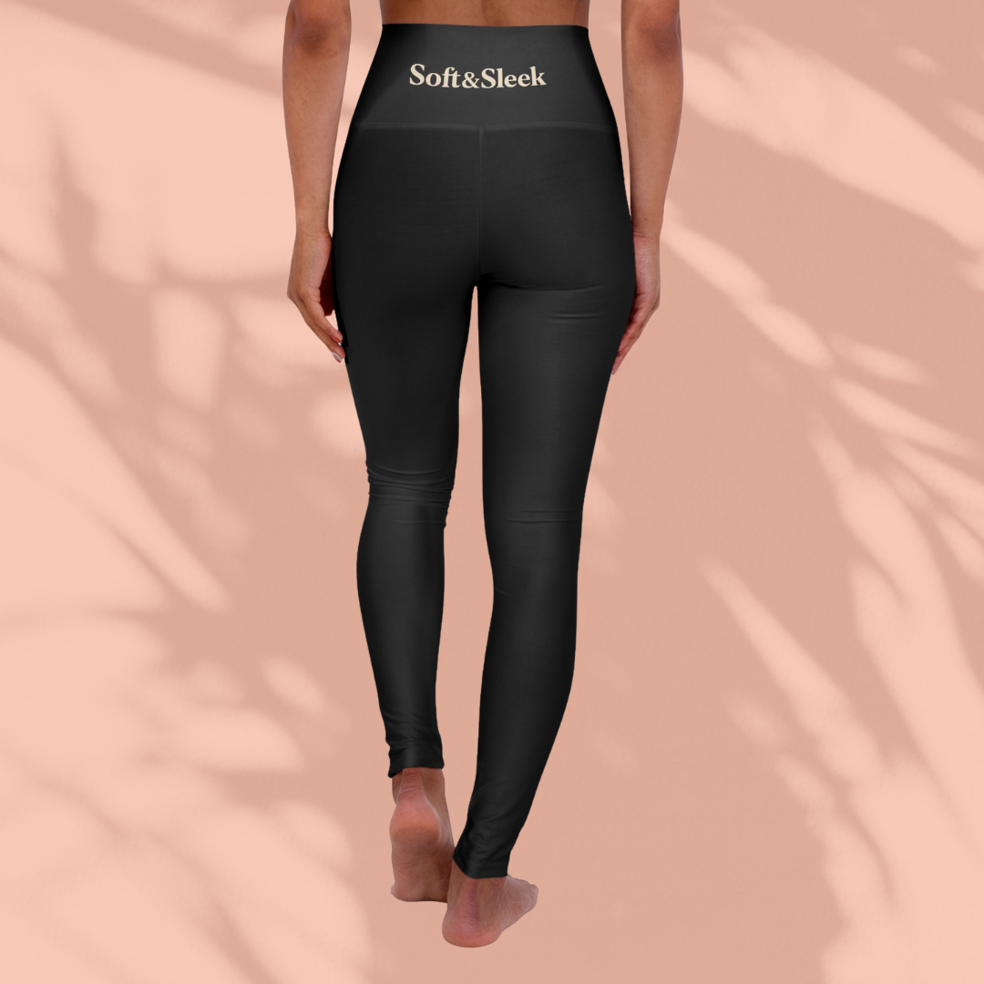 Rear view of a woman in black Soft & Sleek leggings with logo at the waistband, peach background and soft shadows.